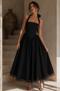 Woman in a black dress standing on a staircase with a neutral background